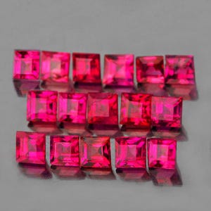 May include: A collection of square-cut, vibrant pink gemstones. The gems are arranged in rows, each with a polished, reflective surface. The color is a deep, saturated pink, with facets catching the light. The gemstones are likely rubies or pink sapphires.