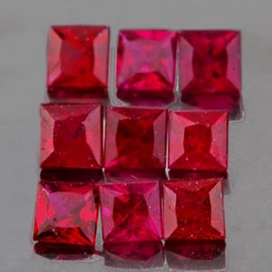 Könnte beinhalten: Zehn quadratische Rubingesteine, jeder mit einer polierten, facettierten Oberfläche. Die Rubine sind tiefrot und in drei Reihen angeordnet.