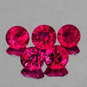 May include: Five round, faceted, ruby red gemstones. The gemstones are arranged in a semi-circle with the two outer gemstones slightly offset from the center.