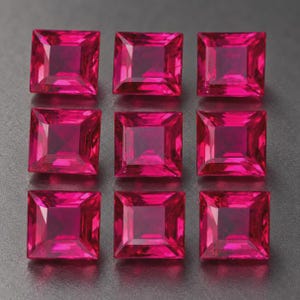 Puede incluir: Nueve piedras preciosas de color rojo fucsia vibrante, con corte cuadrado y dispuestas en una cuadrícula de tres por tres. Cada piedra presenta una superficie facetada que refleja la luz, creando un patrón geométrico de bordes definidos.