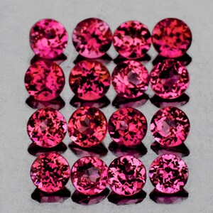 Puede incluir: Una colección de 15 piedras preciosas redondas, facetadas y rosadas. Las piedras preciosas están dispuestas en una cuadrícula sobre una superficie reflectante.