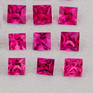 May include: Twelve square-shaped ruby gemstones, each with a deep red color, are arranged in three rows of four on a white surface.