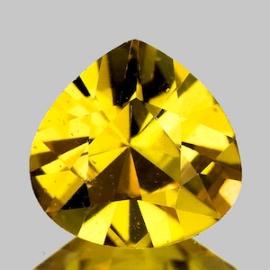 Op de afbeelding: Een gefacetteerde, peervormige edelsteen met een heldere gele kleur. De slijping van de edelsteen onthult talrijke interne facetten, waardoor een steruitbarstingseffect ontstaat. De steen staat tegen een neutrale achtergrond, met een subtiele reflectie eronder.