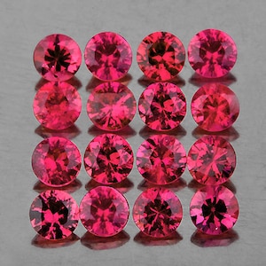 Op de afbeelding: Een verzameling van 15 ronde, gefacetteerde, roze robijn edelstenen. De edelstenen zijn gerangschikt in een rasterpatroon.