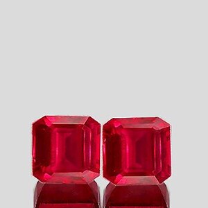Puede incluir: Dos gemas rojas vibrantes, talladas en forma cuadrada. Se presentan sobre un fondo gris claro, con sus reflejos visibles debajo. El corte de las piedras permite la máxima reflexión de la luz, realzando su brillo.