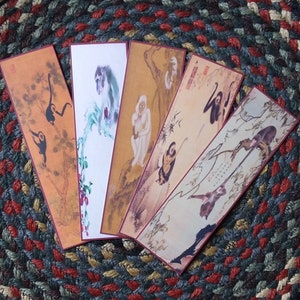 May include: Five colorful bookmarks with images of monkeys and trees. The bookmarks are on a woven rug with brown, green, and red stripes.