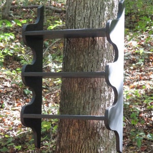 May include: A black wooden shelf with three shelves attached to a tree trunk. The shelf has a decorative, scalloped edge.