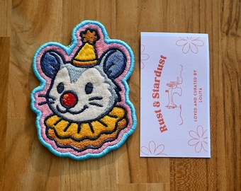 May include: Embroidered patch featuring a cartoon mouse wearing a party hat and ruffled collar. The patch has a pink and blue border. A card with the text "Rust & Stardust" and "Loved and curated by Lolita" is next to the patch.