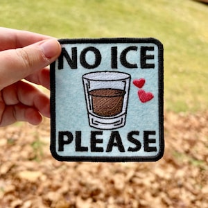 May include: Square patch with the words "NO ICE PLEASE" in black, with a drawing of a drink in a glass and two red hearts. The patch has a black border and a light blue background.