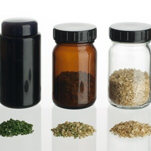 May include: Three glass jars with black lids, two of which are filled with dried herbs. The jars are on a white surface.