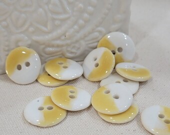 May include: A group of 12 ceramic buttons with a white and yellow gradient. The buttons have two holes each.