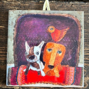 May include: A colorful illustration of two dogs and a bird on a red rug. The dogs are a brown and white French bulldog and a brown dachshund. The bird is red with a yellow beak and is perched on top of the dachshund's head.