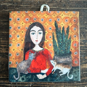May include: A painting of a woman with long brown hair wearing a red shirt and holding two cats. The woman is sitting in front of a plant in a pot. The background is a yellow and orange pattern.