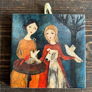 May include: Two women and a dog stand in a forest setting. One woman is wearing a red dress and holding a white dove. The other woman is wearing a yellow dress and holding a birdcage with a white bird inside. The dog is white and gray and is standing next to the woman in the red dress.