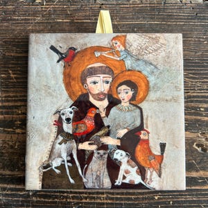 May include: A colorful ceramic tile featuring a painting of Saint Francis of Assisi with animals. The saint is depicted with a brown robe, holding a bird in his hand. He is surrounded by a dog, a cat, a bird, and a small child. The tile has a yellow ribbon attached to the top.