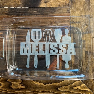 May include: Clear glass baking dish with etched kitchen utensil designs and the name "MELISSA". The rectangular dish has handles on each side. The etched designs include a knife, spatula, whisk, spoon, and rolling pin.