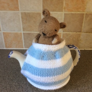 Könnte beinhalten: Eine gestrickte Teekannenhülle in blau-weißen Streifen mit einem braunen, gestrickten Teddybären, der aus der Oberseite schaut.