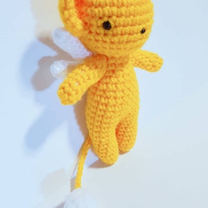May include: A yellow crocheted stuffed animal with white wings and a white tail. The animal has black eyes and a small, round body.