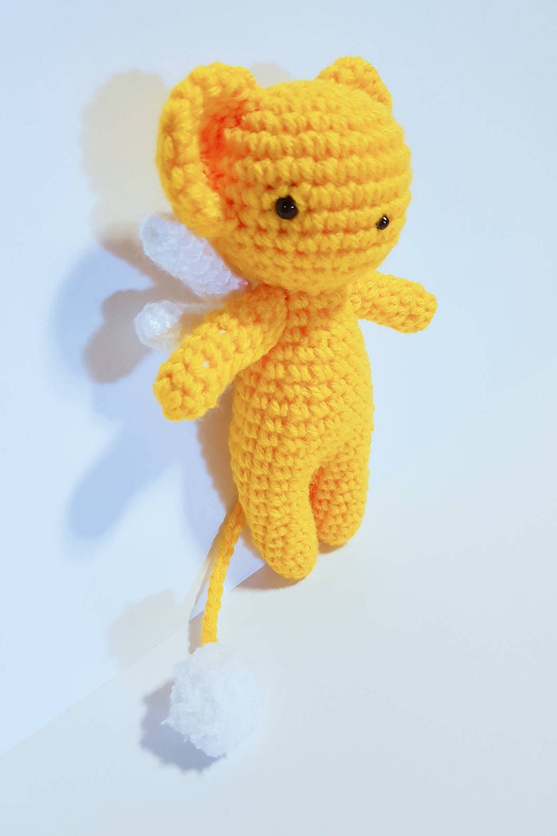 May include: A yellow crocheted stuffed animal with white wings and a white tail. The animal has black eyes and a small, round body.