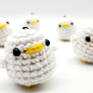 Peut inclure: Cinq oiseaux en crochet blanc avec des yeux noirs et des becs jaunes. Les oiseaux sont disposés en rangée sur une surface blanche.