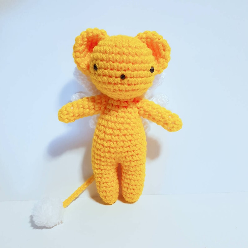 May include: A yellow crocheted plush toy with white wings and a white tail. The toy has a round head with black eyes and a small, pointed nose.