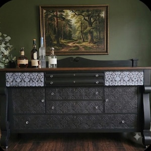 May include: A black wooden sideboard featuring a dark wood top, two upper drawers with clear knobs, and lower cabinet doors and drawers decorated with a black embossed tile pattern. The upper side panels feature a white and black damask print.