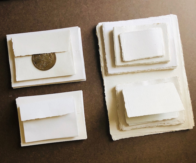 May include: Four stacks of white paper with deckled edges. The top sheet of the stack on the left has a gold coin on it.