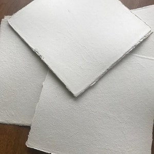 Puede incluir: Tres hojas de papel blanco texturizado con bordes irregulares. El papel es grueso y tiene una superficie rugosa.