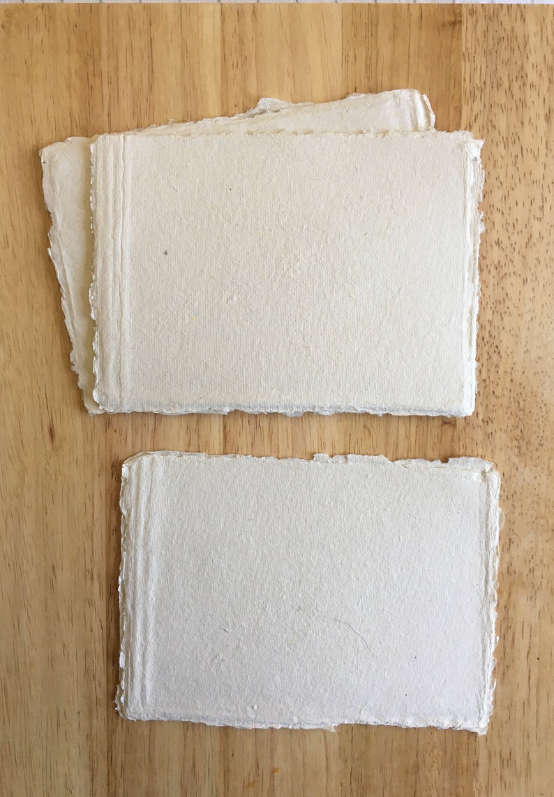 May include: Two sheets of handmade paper with a rough, textured surface. The paper is off-white in color and has a slightly irregular shape.