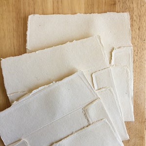May include: A stack of four sheets of handmade paper with deckled edges. The paper is a creamy white color and has a slightly textured surface.