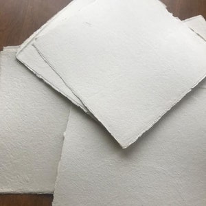 Puede incluir: Una pila de hojas de papel blanco texturizado con bordes irregulares.
