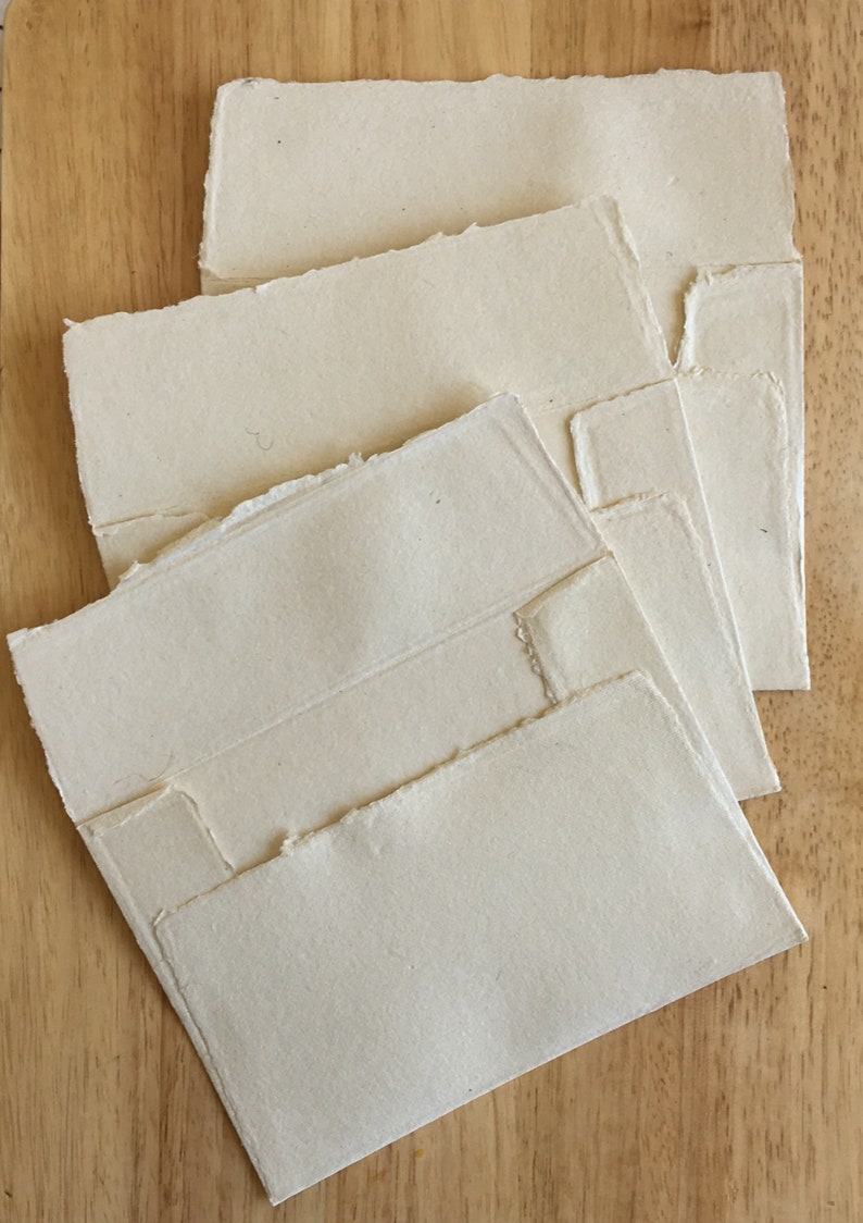 May include: Four white handmade paper envelopes with deckled edges. The envelopes are stacked on top of each other, with the largest envelope on the bottom and the smallest envelope on top.