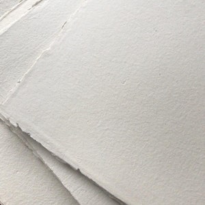 Puede incluir: Una pila de cuatro hojas de papel blanco hecho a mano con bordes irregulares.