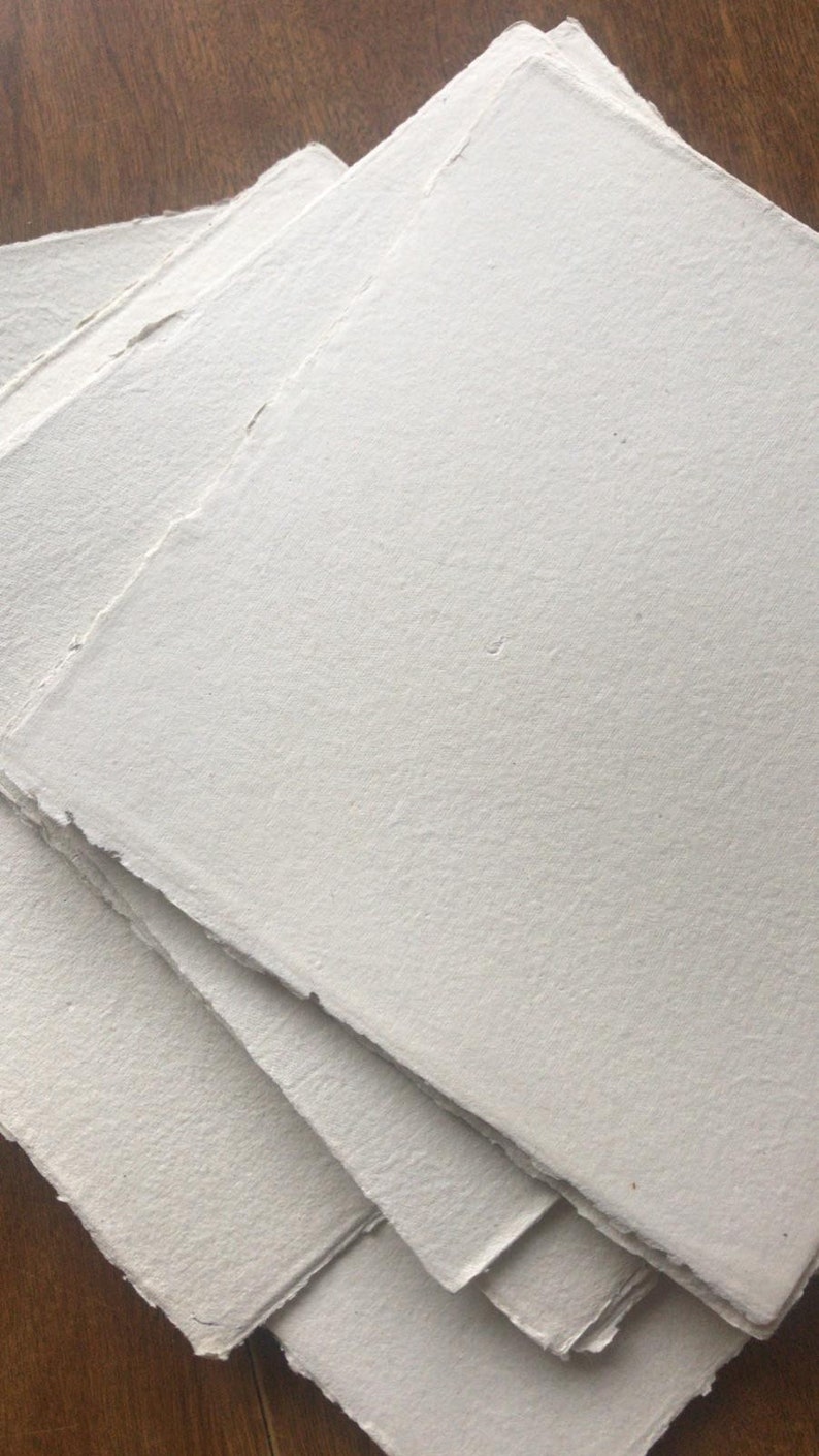 Puede incluir: Una pila de cuatro hojas de papel blanco hecho a mano con bordes irregulares.