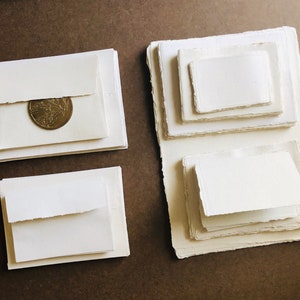 Op de afbeelding: Vier stapels wit papier met onregelmatige randen. Het bovenste vel van de stapel links heeft een gouden munt erop.