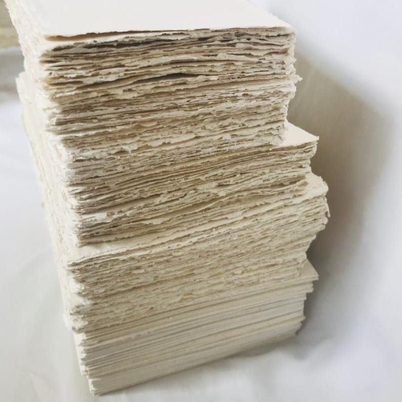 May include: A stack of off-white handmade paper sheets. The paper has a rough, textured surface.