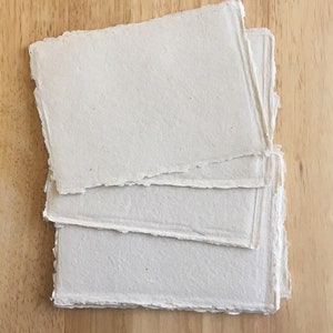 May include: A stack of four sheets of handmade paper with deckled edges. The paper is a light beige color and has a slightly textured surface.