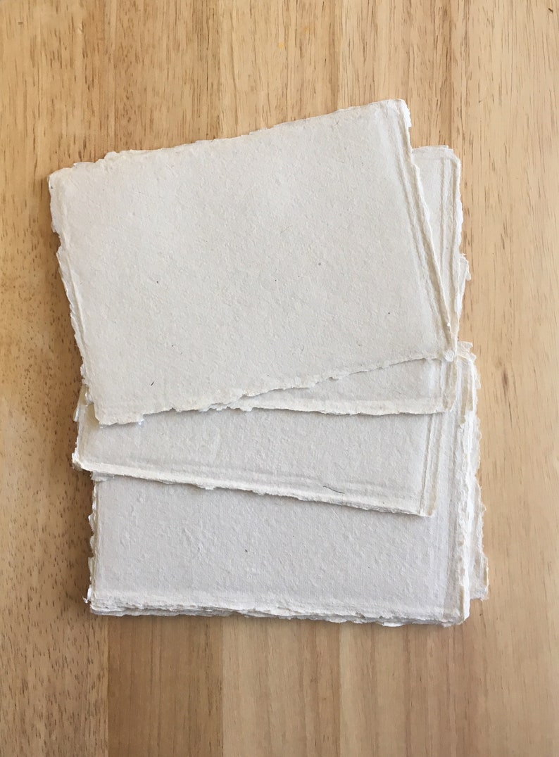 May include: A stack of four sheets of handmade paper with deckled edges. The paper is a light beige color and has a slightly textured surface.