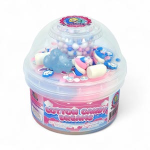 May include: A clear plastic container filled with pink and blue slime, topped with decorative elements. The container is labeled "Cotton Candy Dreams" and includes cloud and marshmallow-shaped decorations. The top section holds small, round, blue and white beads.