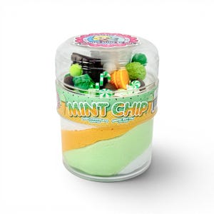May include: A clear plastic jar filled with mint chip-scented slime. The jar has a green and white base with an orange layer in the middle. The top of the jar is filled with small candies and chocolate pieces. The text "Mint Chip" is printed on the jar.