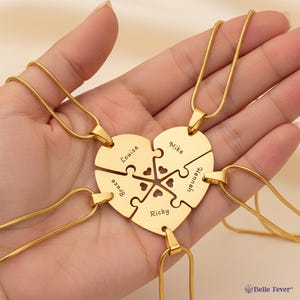 Puede incluir: Un collar dorado con un colgante en forma de corazón hecho de piezas de rompecabezas. Cada pieza está grabada con un nombre: Louise, Bruce, Ricky, Mike y Hannah. El collar tiene una cadena delicada.