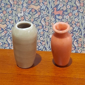 May include: Two small ceramic vases. One is a light beige colour with a smooth surface. The other is a terracotta colour with a slightly textured surface. Both vases have a simple design and are suitable for small floral arrangements.