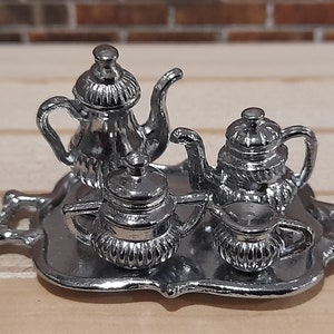 May include: A silver tea set on a silver tray. The set includes a teapot, creamer, sugar bowl, and a teacup.