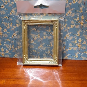 May include: A gold-coloured picture frame with a simple ornate design. The frame is packaged in a clear plastic bag with a hanging hole.