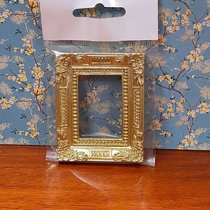 May include: A gold-coloured picture frame with ornate detailing. The frame is packaged in a clear plastic bag with a white hang tag.