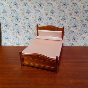 May include: A miniature wooden bed with a pink satin headboard and mattress. The bed is sitting on a wooden surface.