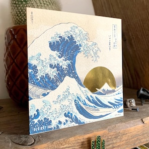 May include: A print of the Great Wave off Kanagawa by Katsushika Hokusai, a famous Japanese woodblock print. The wave is depicted in blue and white, with Mount Fuji in the background. The sun is a gold circle.