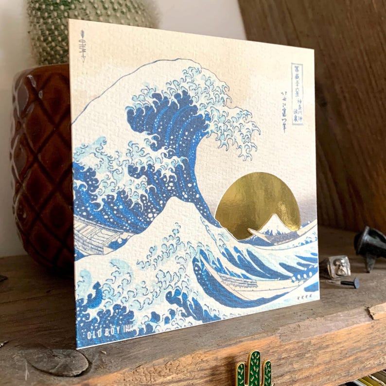 May include: A print of the Great Wave off Kanagawa by Katsushika Hokusai, a famous Japanese woodblock print. The wave is depicted in blue and white, with Mount Fuji in the background. The sun is a gold circle.