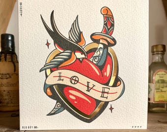 May include: A square art print with a traditional tattoo design. It features a red heart pierced by a dagger, a swallow bird, and a banner with the word "LOVE." The design includes gold accents and the text "OLD BOY INK."