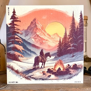 Könnte beinhalten: Quadratischer Druck mit einem Cowboy auf einem Pferd in einer Berglandschaft bei Sonnenuntergang. Im Vordergrund brennt ein Lagerfeuer. Der Druck hat einen Vintage-Aquarellstil und den Text "OLD BOY INK." unten links.